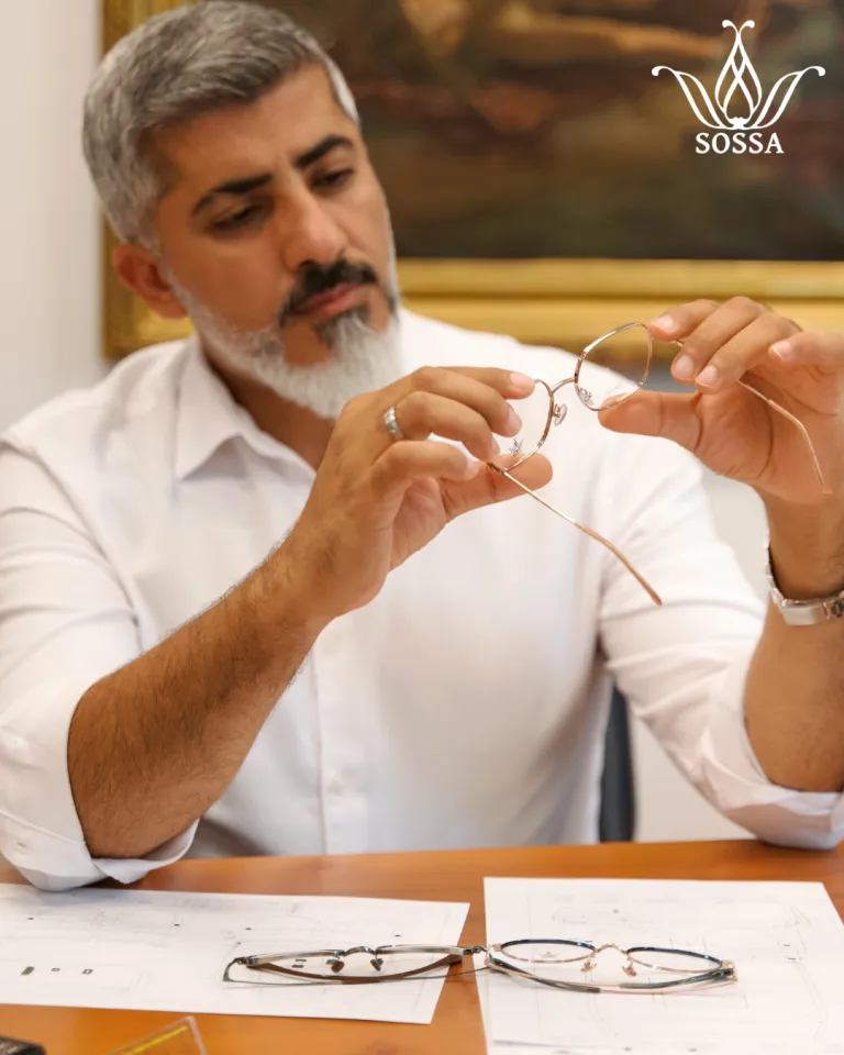 Ali Kemal in a white shirt inspecting a thin metal SOSSA frame at his design desk